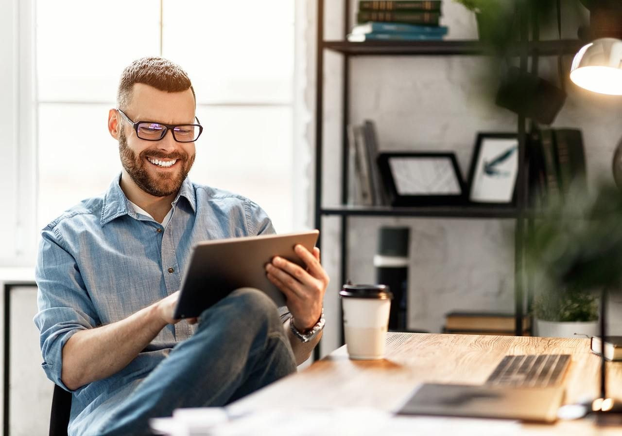 A smiling man in glasses is using a tablet.